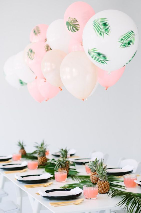 a fun tropical bridal shower tablescape with a tropical leaf table runner, pineapples, gold cutlery and pink and white balloons