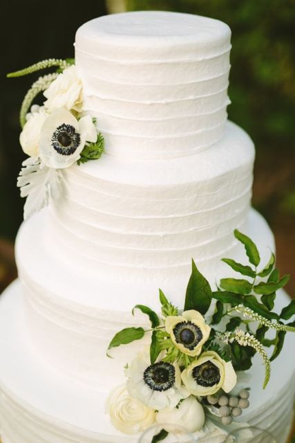 an elegant white buttercream wedding cake decorated with greenery and anemones is a chic and stylish spring or summer wedding idea