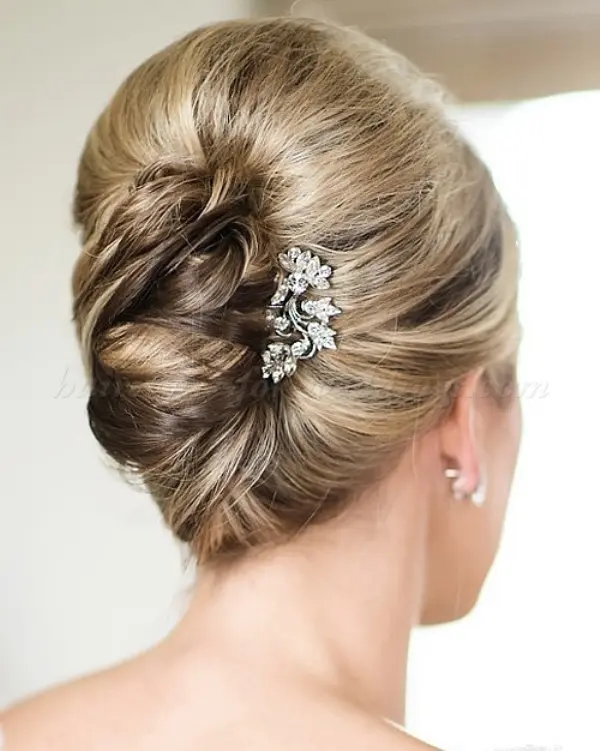 a very formal and refined French twist updo with a volume on top and a rhinestone brooch for an accent
