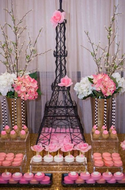 a glam Parisian themed bridal shower sweets table with various pink sweets, white and pink blooms and an Eiffel Tower as a centerpiece
