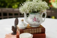 a stylish centerpiece of a couple of vintage books, a teacup, a teapot with baby’s breath and a pink doily