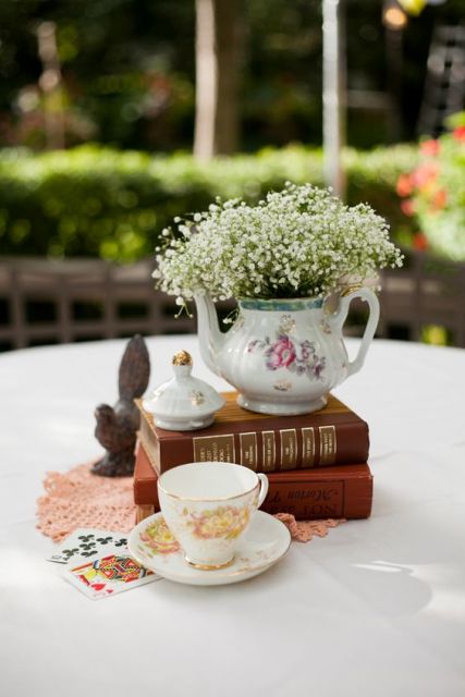 a stylish centerpiece of a couple of vintage books, a teacup, a teapot with baby's breath and a pink doily