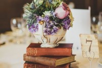 a stylish wedding centerpiece of a stack of books, a teapot with purple and pink flowers and greenery