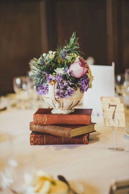 a stylish wedding centerpiece of a stack of books, a teapot with purple and pink flowers and greenery