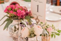 a bright and fun centerpiece of a silver teapot and coffee pit used as vases for blush and hot pink blooms and a table number