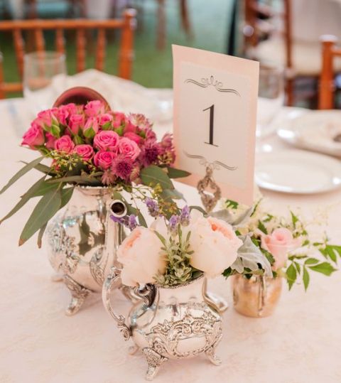 a bright and fun centerpiece of a silver teapot and coffee pit used as vases for blush and hot pink blooms and a table number