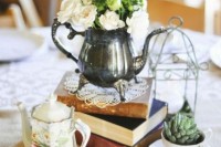 a catchy vintage centerpiece of a stack of books, a silver teapot with blooms, a potted succulent, a cage and a coffee pot