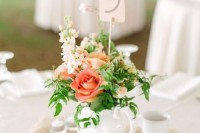 a white teapot with coral and blush blooms plus greenery and a table number on a stand
