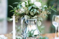 a vintage wedding centerpiece of a silver teapot, a glass and a candle holder plus a single white candle