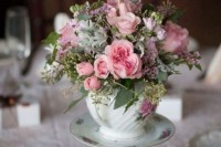 floral vintage teacups and a teapot on top with usual and pale greenery, pink blooms and and a topped with macrame and a table number