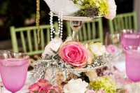 an eye-catchy wedding centerpiece of a mirror, a couple of stands, bright blooms, greenery, pearls and a teapot on top