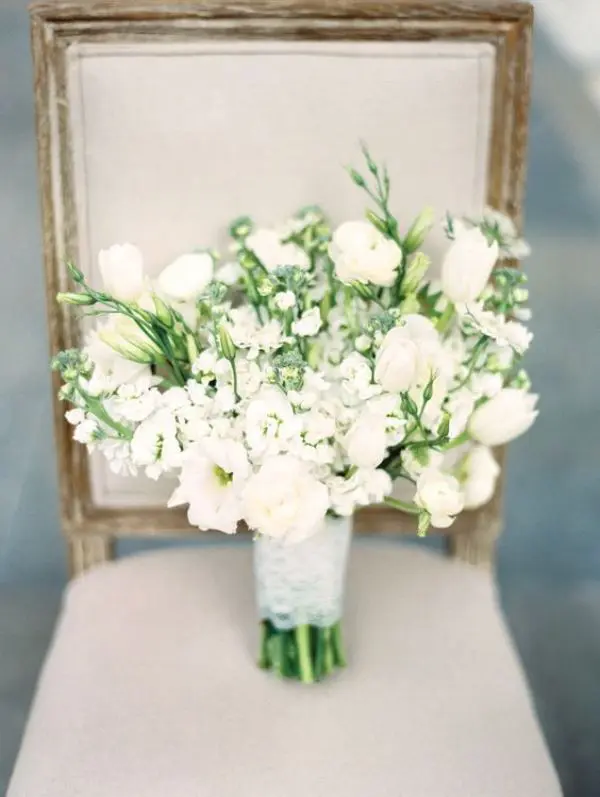 white tulips, smaller white blooms, greenery and peonies in a bouquet with a white wrap