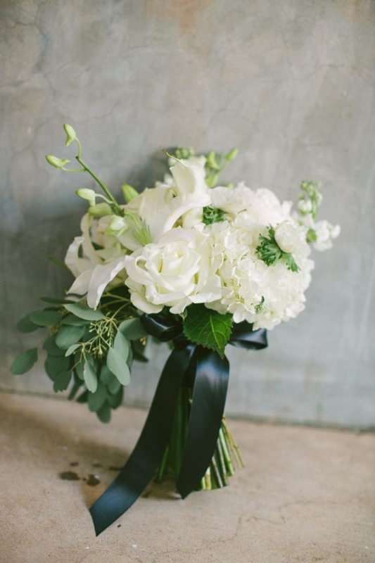 a textural white wedding bouquet with greenery, a dark green bow and much dimension