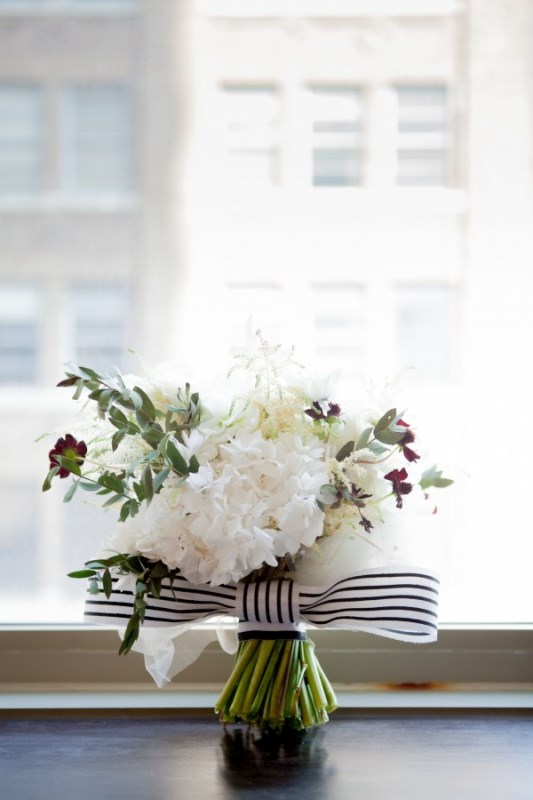a white wedding bouquet spruced up with greenery and touches of burgundy blooms plus a striped bow