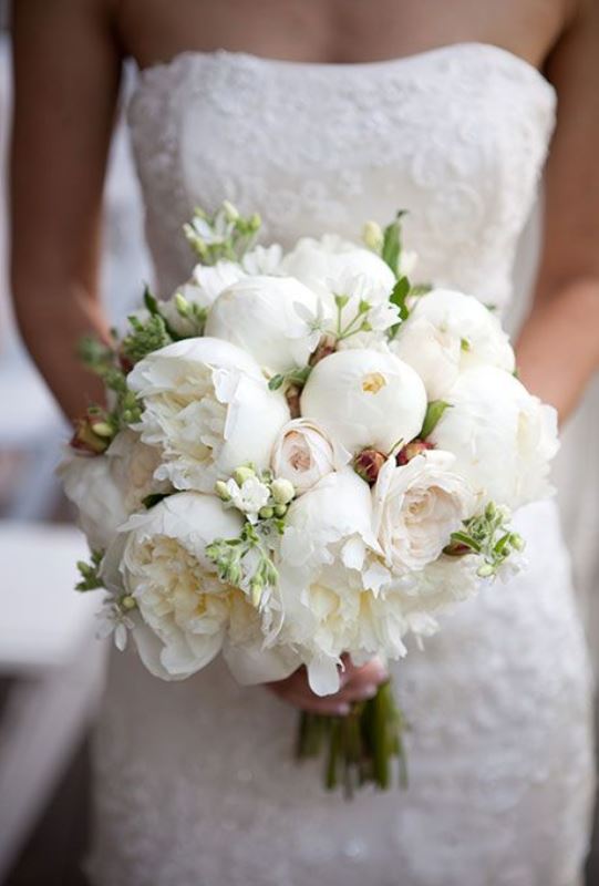 a white peony wedding bouquet with smaller blooms and greenery shaped as a ball
