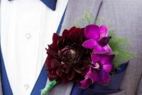 a colorful wedding boutonniere of purple orchids and a deep burgundy dahlia plus greenery for a bright or moody fall wedding