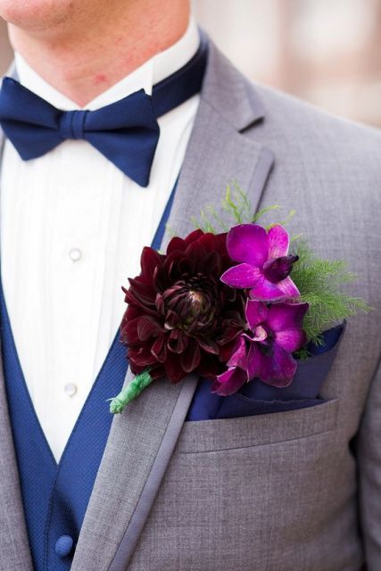 a colorful wedding boutonniere of purple orchids and a deep burgundy dahlia plus greenery for a bright or moody fall wedding