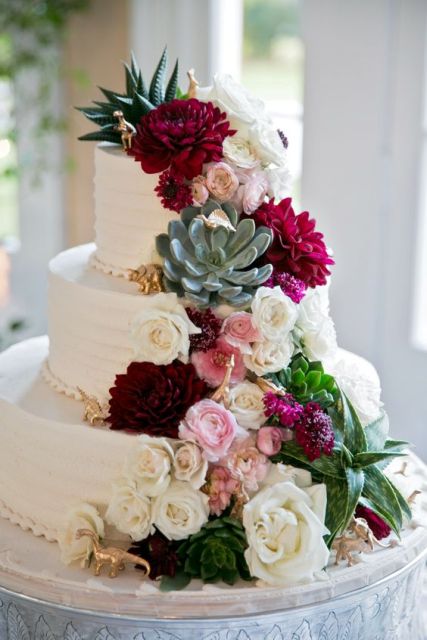 a white wedding cake decorated with white and pink blooms, succulents, greenery and burgundy dahlias is an amazing dessert for a contrasting wedding