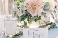 a beautiful pastel wedding centerpiece that includes blush dahlias, white blooms and pale greenery and is paired up with candles for a spring or summer wedding