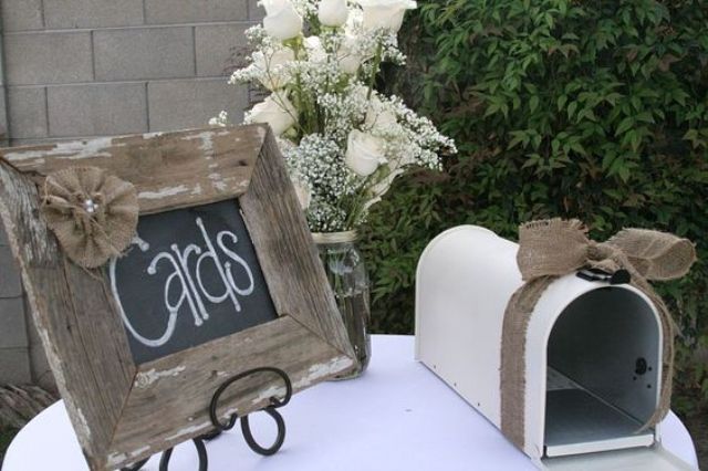 a rustic setting with a white mailbox decorated with burlap, a chalkboard sign in a wooden frame and with burlap flowers