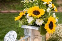 a water can with greenery with sunflowers is a cool idea  to decorate your summer or fall wedding