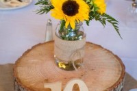 a wood slice, a table number, a jar with sunflowers and greenery for a rustic wedding