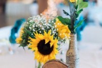a wood slice, a slice table number, a bottle wrapped with yarn and sunflowers and baby’s breath