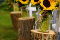 jars with sunflowers placed on tree stumps are cool rustic aisle liners for a summer wedding