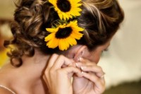 a wavy low updo with some curls down and sunflowers tucked in to embrace the wedding season and theme
