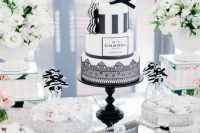 a Parisian-themed bridal shower sweets table with white blooms and greenery, pearls, white meringues and a black and white cake