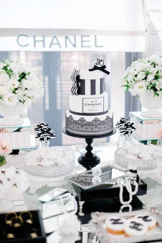 a Parisian themed bridal shower sweets table with white blooms and greenery, pearls, white meringues and a black and white cake