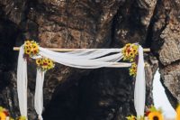 a beach wedding ceremony space done with white fabric and lots of sunflowers for a breezy and cheerful look
