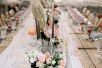 a beautiful wedding table runner of whiet fabric, candles, an air plant, blush and white blooms and greenery, driftwood, tall and thin candles and pampas grass
