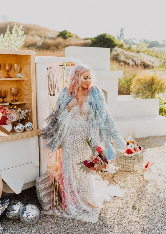 a boho bridal look with a boho lace sheath wedding dress, a silver fringe coverup and pastel pink wavy hair down