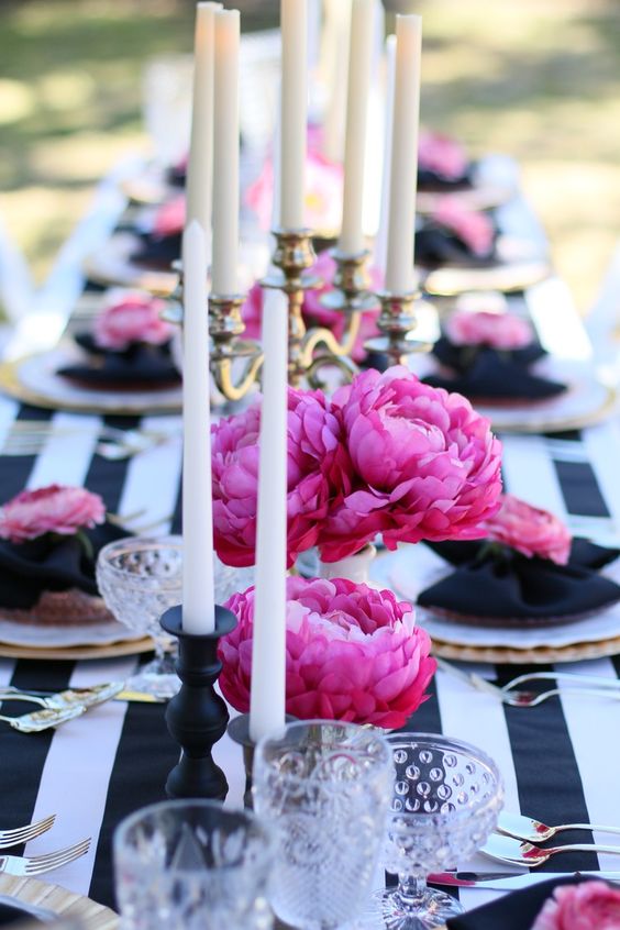 a bold Parisian themed bridal shower tablescape with a striped tablecloth, bold pink peonies, tall and thin candles and gold cutlery
