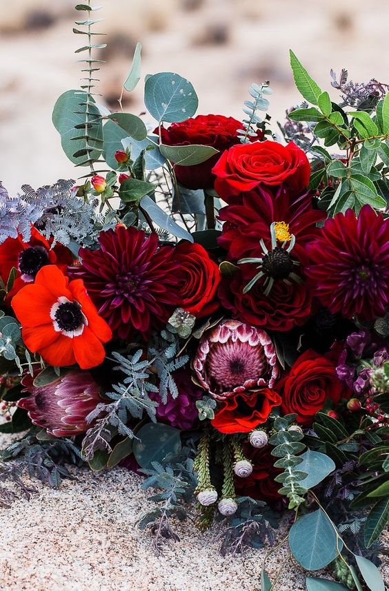 a bold and catchy wedding centerpiece of red anemones, red roses and burgundy dahlias, greenery and berries for a bold wedding