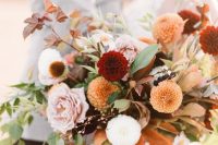 a bold autumn wedding bouquet with orange, white and burgundy dahlias, blush roses, greenery and bold fall leaves