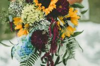 a bold fall wedding bouquet of deep purple dahlias, sunflowers, baby’s breath, greenery of various kinds is a very chic idea