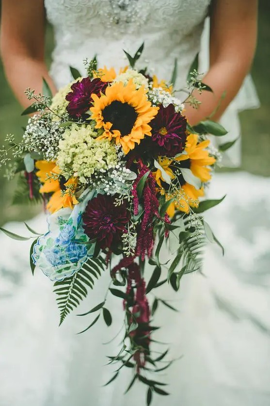 a bold fall wedding bouquet of deep purple dahlias, sunflowers, baby's breath, greenery of various kinds is a very chic idea