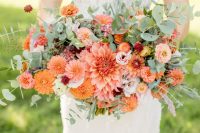 a bold summer wedding bouquet composed of orange and pink dahlias, pink ranunculus, smaller fillers and greenery