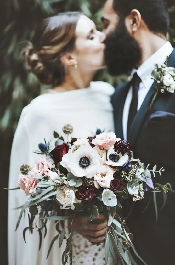 a bold winter wedding bouquet of burgundy and pink roses, white anemones, greenery, thistles and eucalyptus is wow
