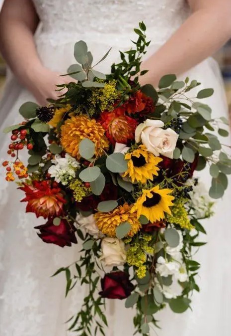 a bright cascading wedding bouquet of sunflowers, red and yellow dahlias, white and burgundy roses, greenery and berries