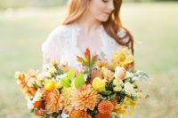 a bright fall wedding bouquet of orange and yellow dahlias, pink and yellow ranunculus and roses, greenery and fall leaves