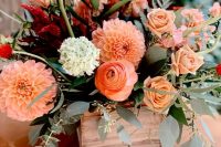 a bright fall wedding centerpiece of a wooden box with greenery, orange dahlias, ranunculus, greenery and some neutral blooms