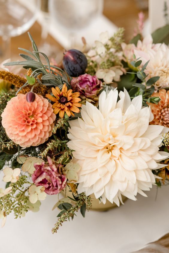 a bright fall wedding centerpiece of pink, yellow blooms, white and orange dahlias, dried flowers and greenery, figs