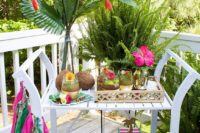 a bright tropical bridal shower cart with coconuts, tropical greenery, colorful tassels and bold blooms
