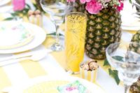 a bright tropical bridal shower table setting with pineapples with bright florals and pink flamingos, yellow glasses and plates and printed napkins