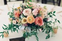 a bright wedding centerpiece of blush roses, pink and yellow ranunculus, orange dahlias, waxflower and greenery plus candles around