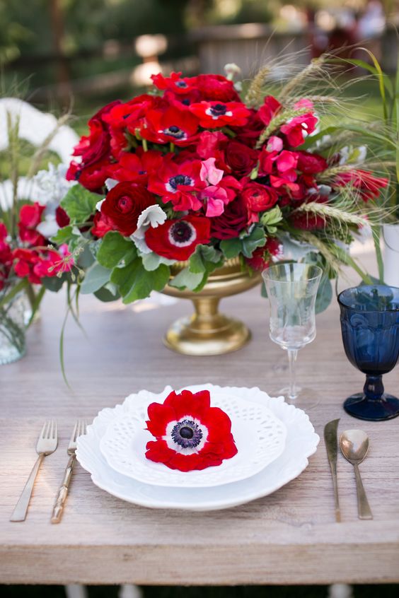 a bright wedding centerpiece of red anemones and ranunculus, greenery and grasses for a bold wedding
