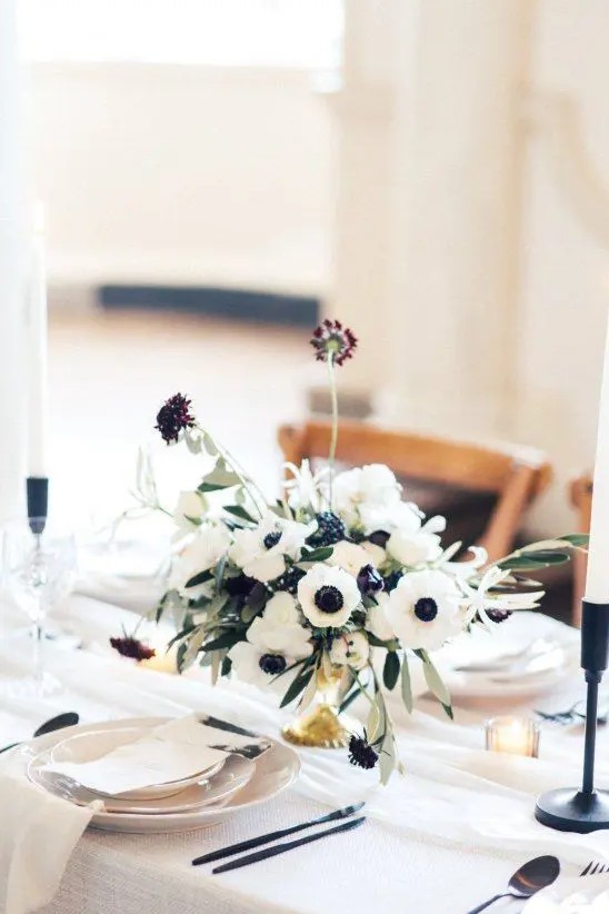 a catchy wedding centerpiece of white anemones and dark purple blooms plus some greenery and candles around is amazing
